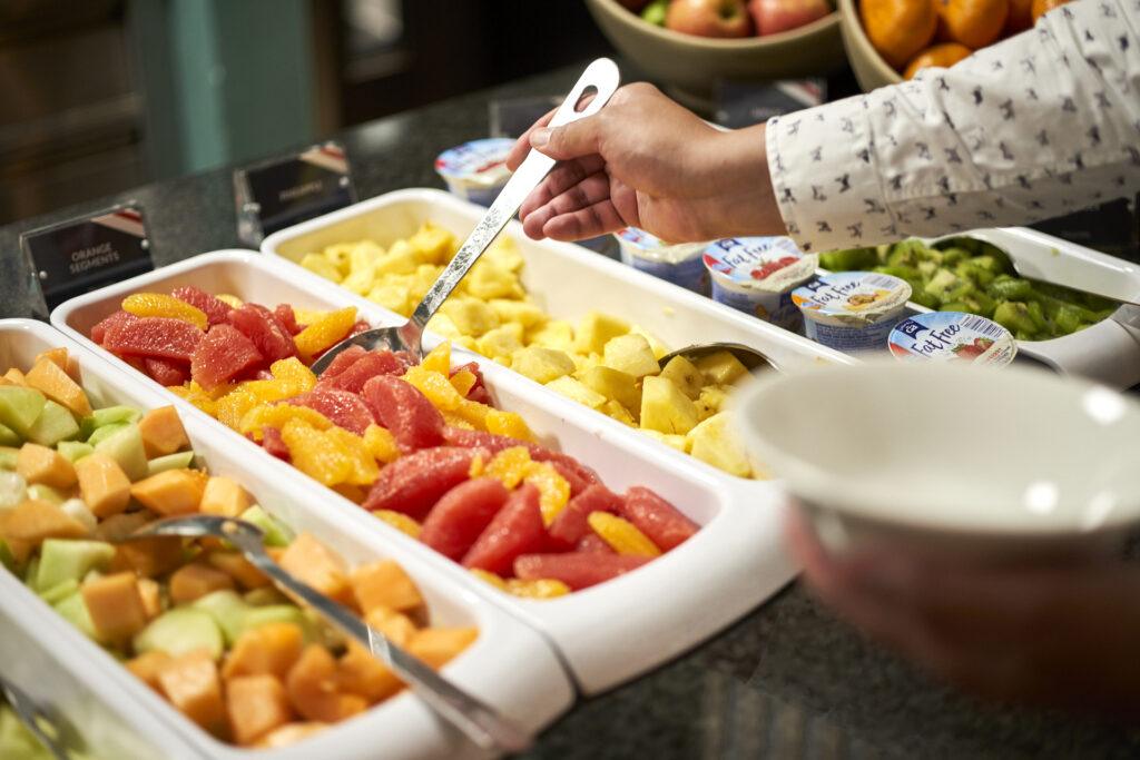 Person choosing fruit at a breakfast buffet
