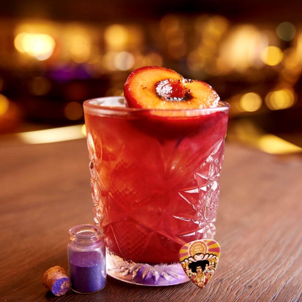 Red cocktail in glass with a peach on top