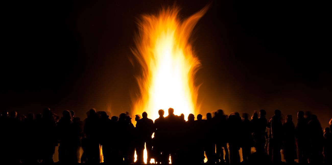 People watching a bonfire at night, slight motion blur to people and the fire