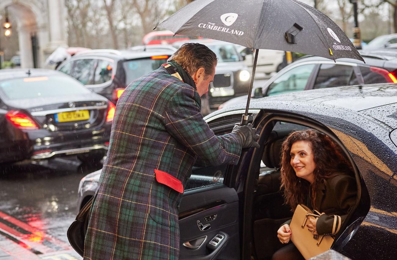 Doorman holding a Cumberland umbrella over a guest stepping out of a car in the rain.