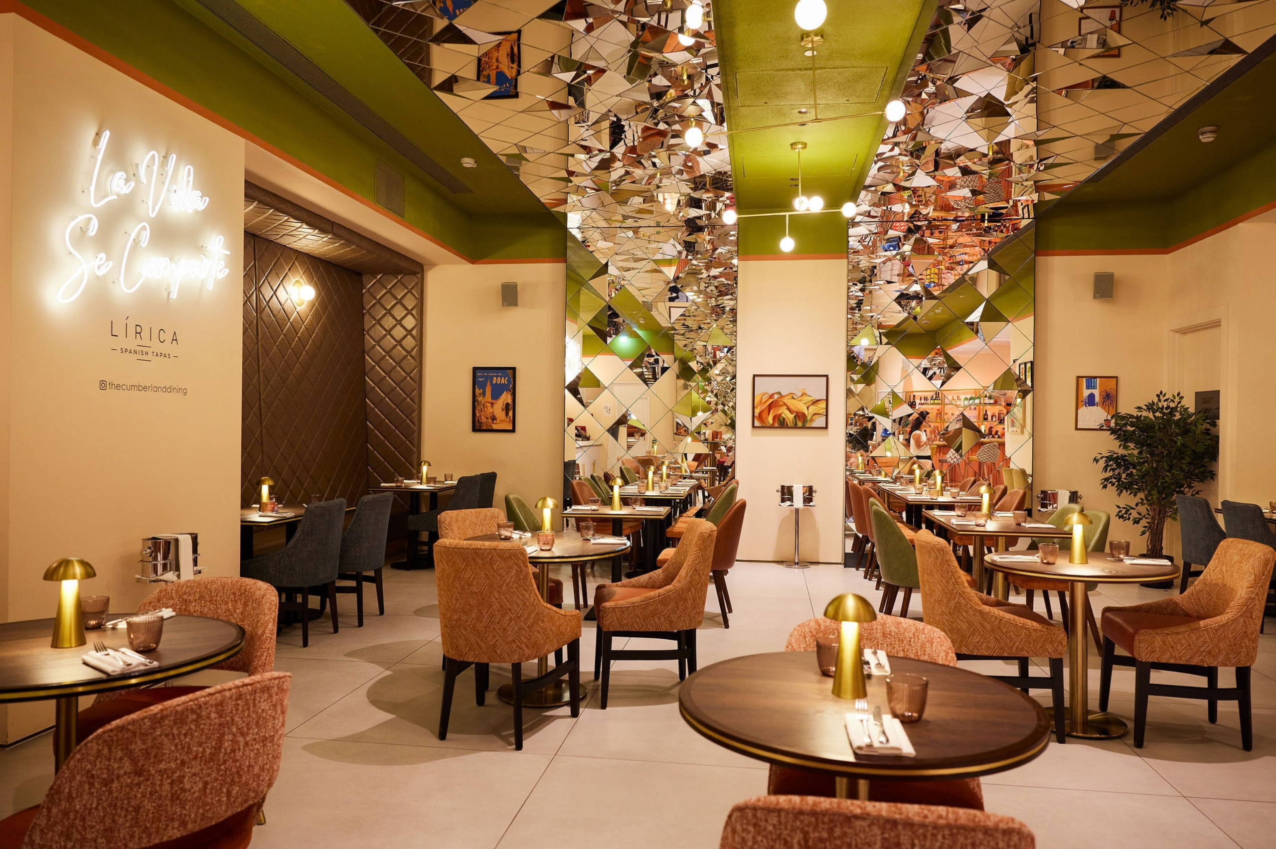 Elegant restaurant interior at Lirica, featuring contemporary seating, mirrored ceiling details, warm lighting and neatly set dining tables.