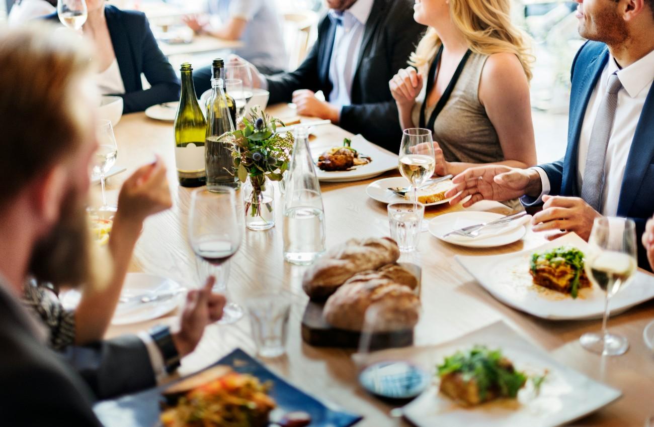 Three colleagues chatting over lunch and wine at a restaurant table.