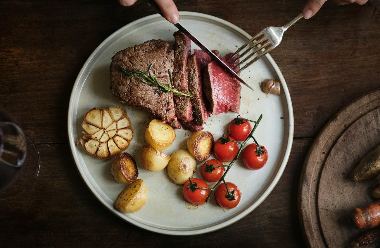 Sliced steak served with roasted potatoes, vine tomatoes, garlic and rosemary on a ceramic plate.