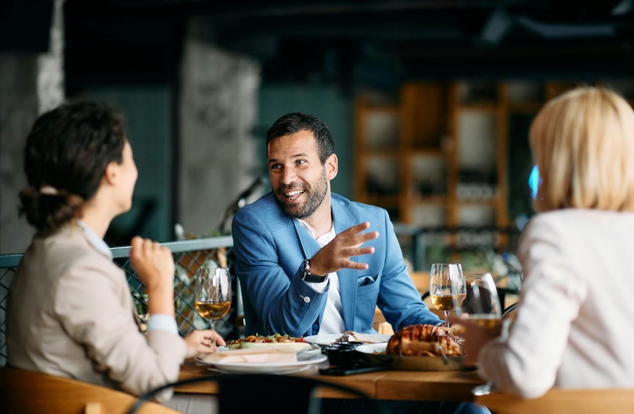 Business diners sharing a meal around a table set with plated dishes, wine glasses and fresh bread.